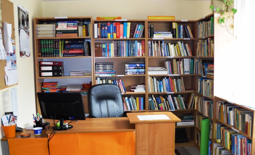 Regały z książkami, w tle komputer dla pracownika biblioteki